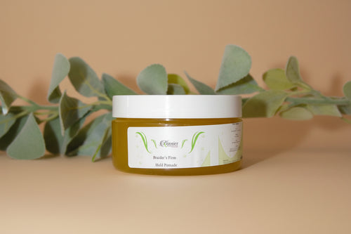 Two jars of a product with a label, surrounded by eucalyptus leaves on a white surface.