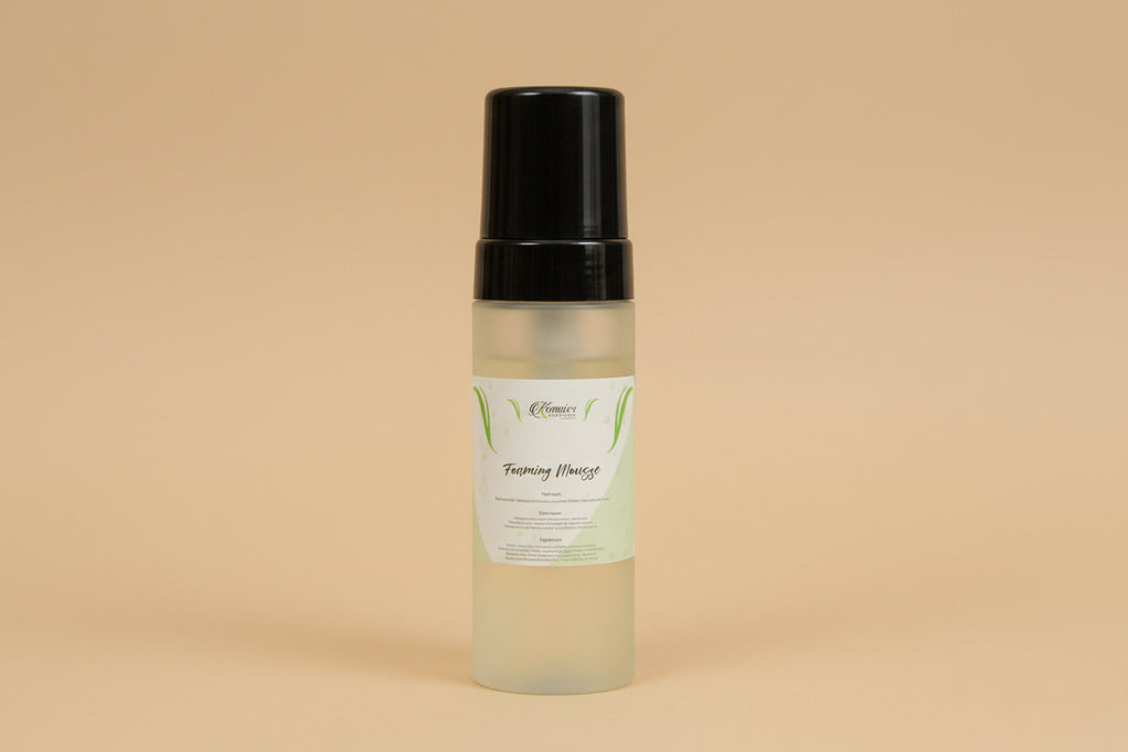 Skincare bottle with black cap and white label on a reflective surface with flowers in the background